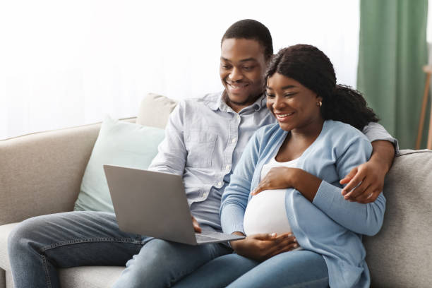 A happy pregnant Nigerian couple sitting on a sofa, looking at each other and smiling, representing a healthy and supported pregnancy journey with nipt in nigeria